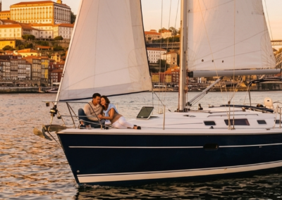 Pareja disfrutando de un paseo romántico en velero por el río Duero con vistas al puente de Don Luis I y la ciudad de Oporto al atardecer