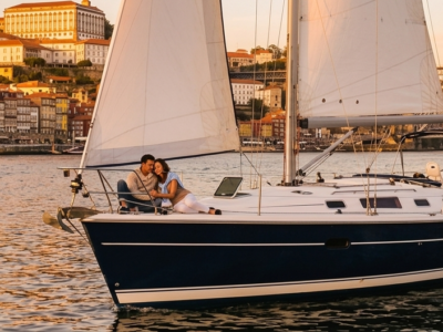 Pareja disfrutando de un paseo romántico en velero por el río Duero con vistas al puente de Don Luis I y la ciudad de Oporto al atardecer