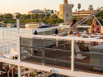Grupo de turistas disfrutando de un tour privado en barco por el río Guadalquivir en Sevilla con la Torre del Oro al fondo al atardecer