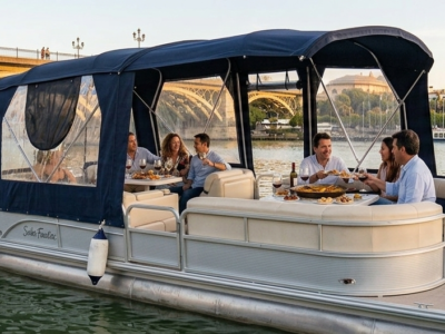 Personas disfrutando de paella y vino en un barco privado por el río Guadalquivir con el puente de Triana y la Torre del Oro.