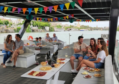 Grupo de personas disfrutando de un tour en barco por el río Guadalquivir en Sevilla con tapas y bebidas.