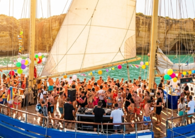 Barco de fiesta con personas disfrutando de música y bebidas frente a los acantilados del Algarve en Vilamoura