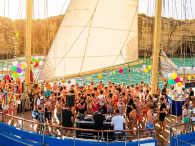 Barco de fiesta con personas disfrutando de música y bebidas frente a los acantilados del Algarve en Vilamoura