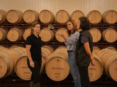 Tres mujeres catan vino tinto rodeadas de barricas de roble en la bodega Vegamar durante una visita guiada en Valencia.
