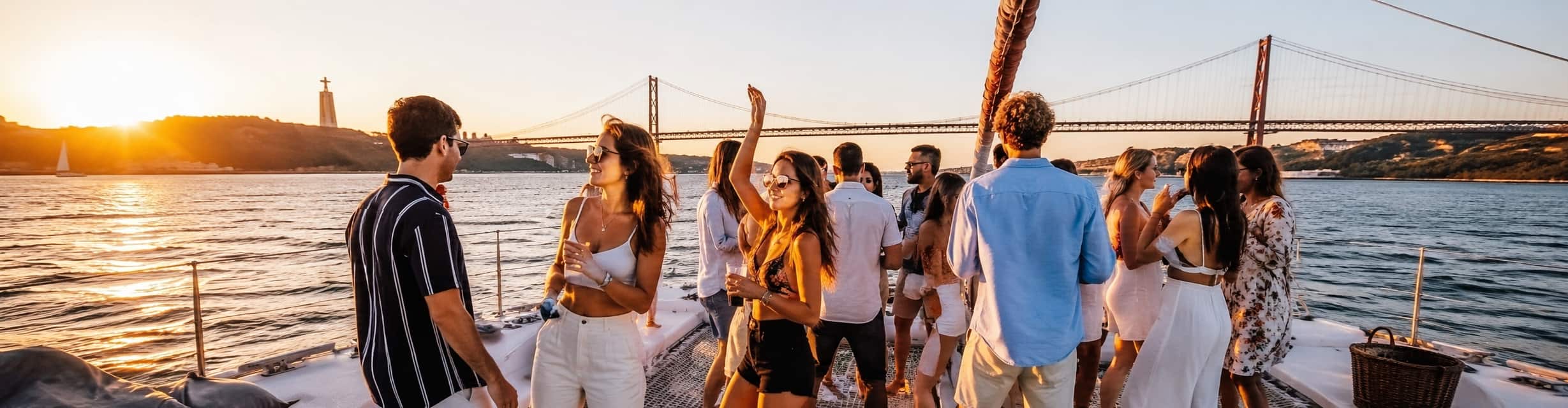 Grupo celebrando en una boat party al atardecer por el río Tajo con el Puente 25 de Abril de fondo · TiToTravel